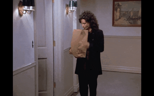 a woman in a black coat holds a brown paper bag
