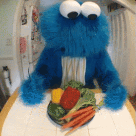 a cookie monster is sitting at a table with a plate of vegetables