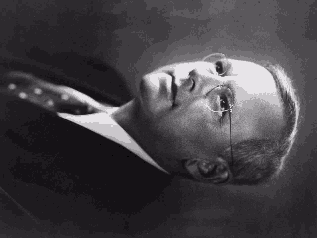 a black and white photo of a man wearing glasses and a suit and tie