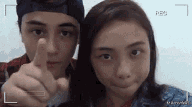 a boy and a girl are standing next to each other and the girl is pointing at the camera
