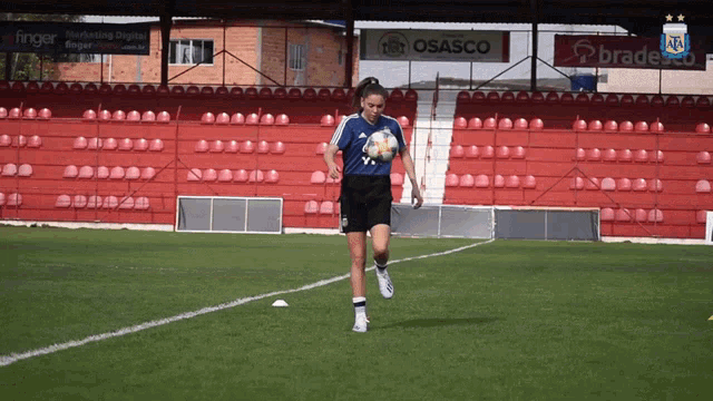 a female soccer player kicks a ball on a field with ads for osanco and bradesco