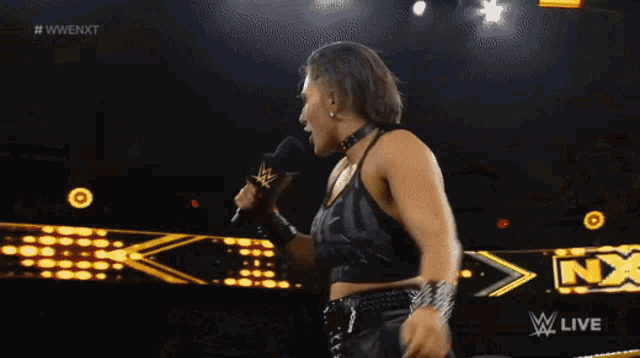 a woman is standing in a wrestling ring with a microphone in her hand and the words w live on the bottom