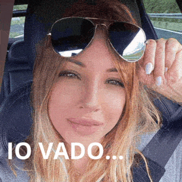a woman wearing sunglasses is sitting in a car with the words " io vado " on the bottom