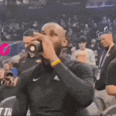 a man in a black nike shirt is drinking from a cup while sitting in the stands .