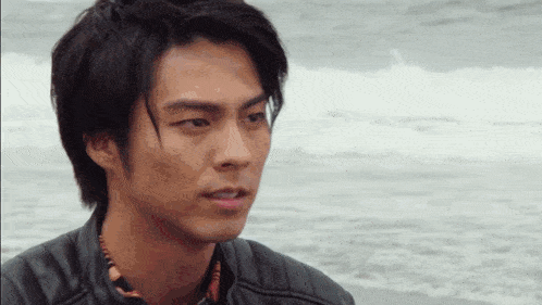a man in a leather jacket is standing on the beach