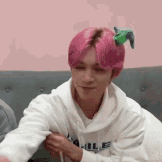 a man with pink hair is wearing a white hoodie and a green bow on his head .