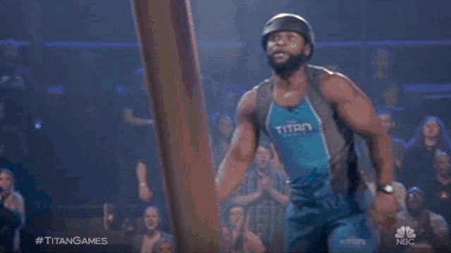 a man climbs a pole with the hashtag #titangames