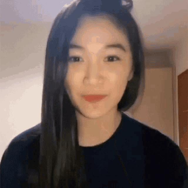 a young woman with long black hair is wearing a black sweater and smiling .