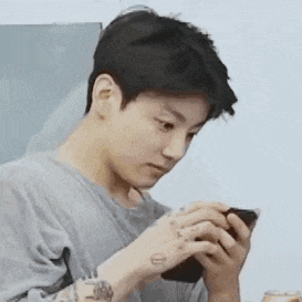 a young man with a tattoo on his arm is holding a cell phone .