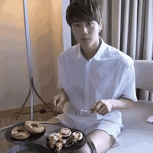 a man in a white shirt is sitting on a bed eating a plate of food .