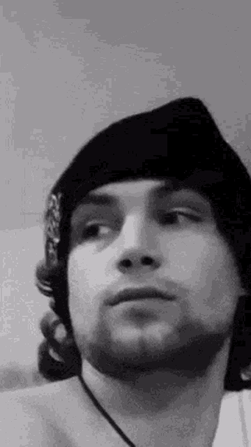 a black and white photo of a young man wearing a beanie and a necklace .