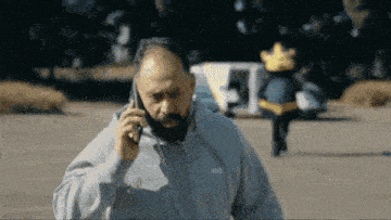 a man with a beard is talking on a cell phone while wearing a hoodie that says hugo