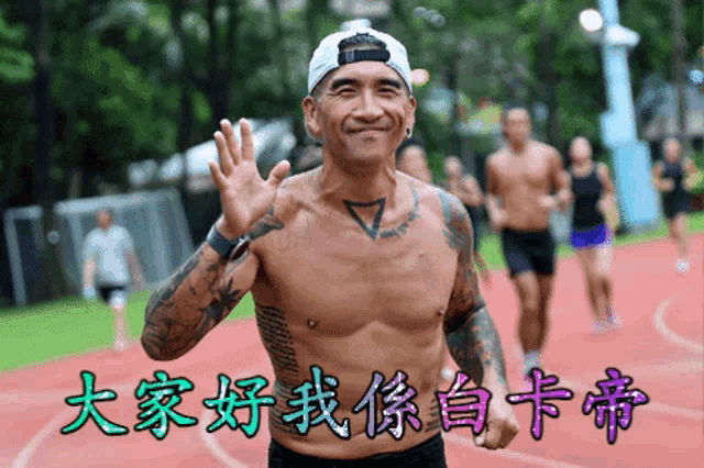 a shirtless man with a tattoo on his chest waves his hand