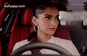 a woman is sitting in the driver 's seat of a car with a steering wheel .