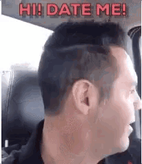 a man is sitting in a car with the words `` hi ! date me ! '' written on his head .