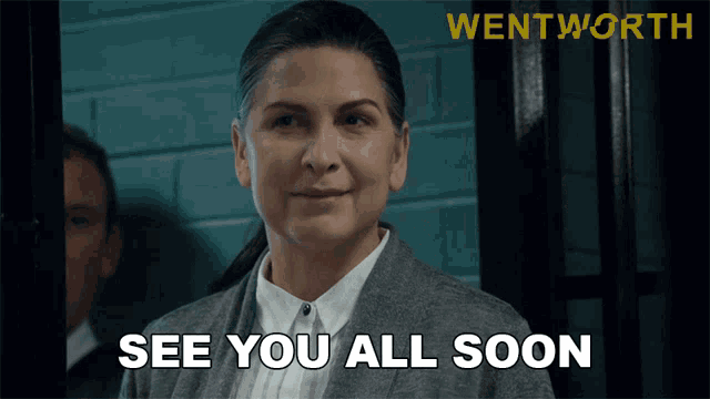 a woman says see you all soon in front of a brick wall