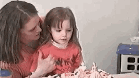 a woman is holding a little girl in her arms while they look at a birthday cake .