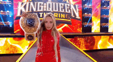 a woman in a red dress is holding a wrestling championship belt while standing on a stage .