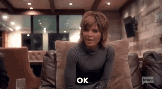 a woman is sitting on a couch in a living room and saying `` ok '' .