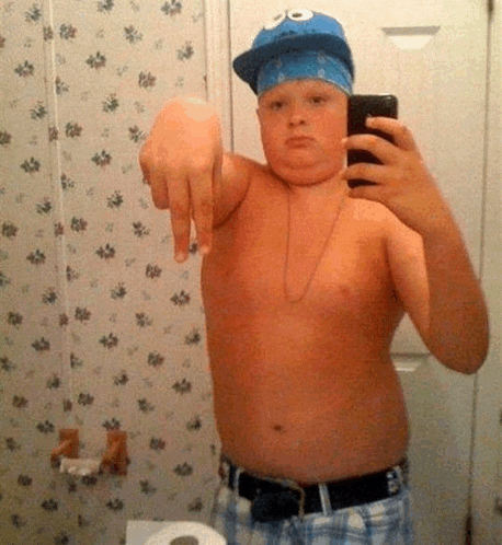 a young boy is taking a selfie in a bathroom while wearing a cookie monster hat and bandana .
