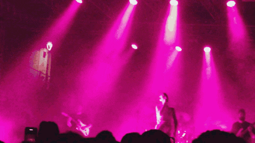 a woman singing into a microphone on a stage surrounded by pink lights