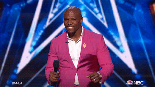 a man in a pink suit is holding a microphone on a stage with the nbc logo in the background