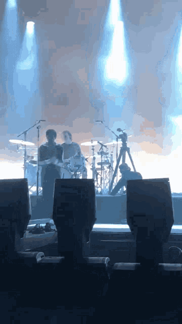 a man playing drums stands next to a man playing a guitar on a stage