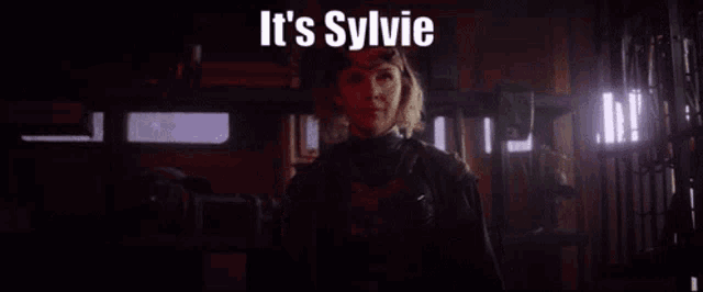 a woman is standing in a dark room with the words `` it 's sylvie sylvie sunday '' .