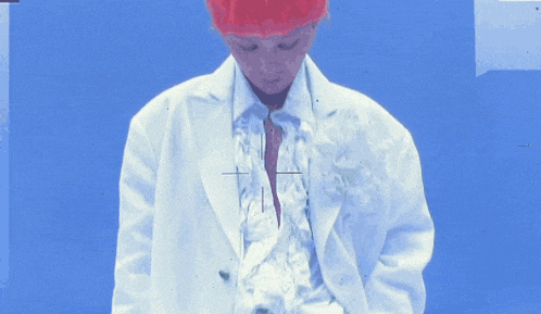 a person wearing a white jacket and a red hat stands in front of a blue background