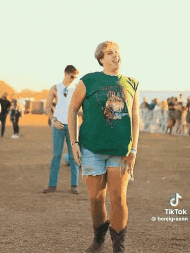 a man in a green shirt and shorts is standing in a field with a crowd behind him .