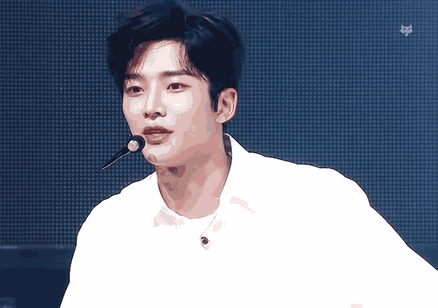 a young man wearing a white shirt and a microphone looks at the camera