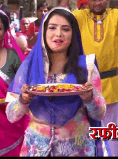 a woman in a blue scarf is holding a plate of food in her hands