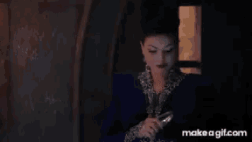 a woman in a blue dress is holding a glass of wine and talking to someone .
