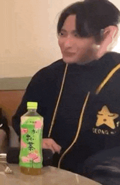 a young man is sitting at a table with a bottle of green tea .