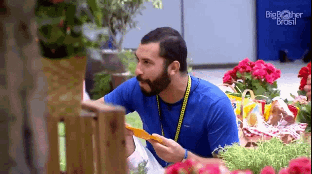 a man in a blue shirt is holding a piece of paper in front of flowers .