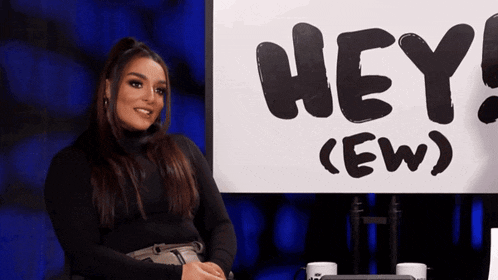 a woman sits in front of a sign that says hey