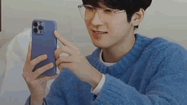 a man wearing glasses and a blue sweater is holding a cell phone in his hand .