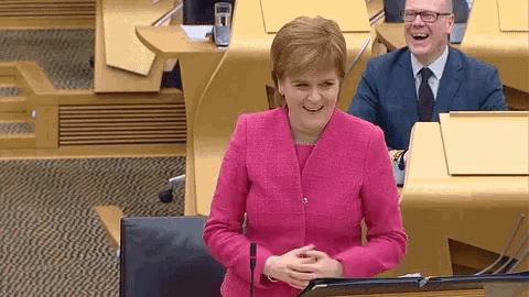 a woman in a pink jacket is smiling in front of a podium