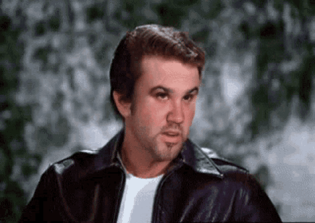 a man wearing a leather jacket and a white shirt is making a face