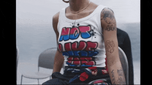 a woman with tattoos on her arm wears a white tank top that says hot like