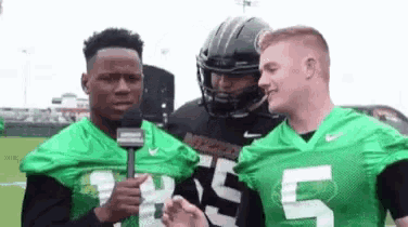 a group of football players are standing next to each other on a field talking to a reporter .