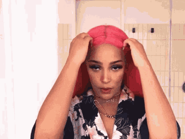 a woman with long pink hair is wearing a floral shirt and a necklace .