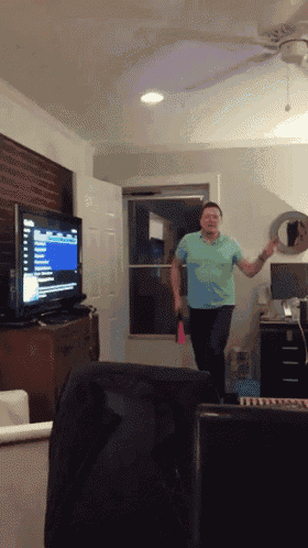 a man in a green shirt is dancing in front of a television