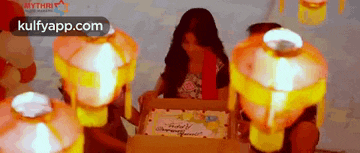 a woman is sitting in front of a birthday cake surrounded by lanterns