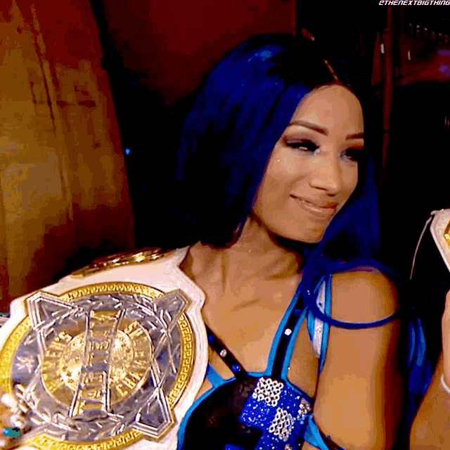 a woman with blue hair is smiling and holding a championship belt