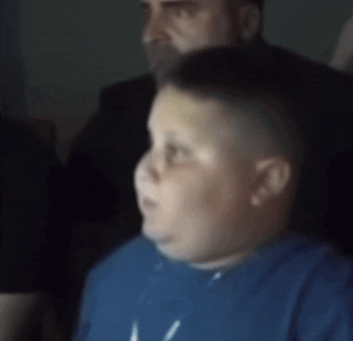 a boy in a blue shirt is looking at something in a dark room
