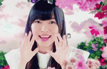 a woman is smiling and making a heart shape with her hands in front of pink flowers .
