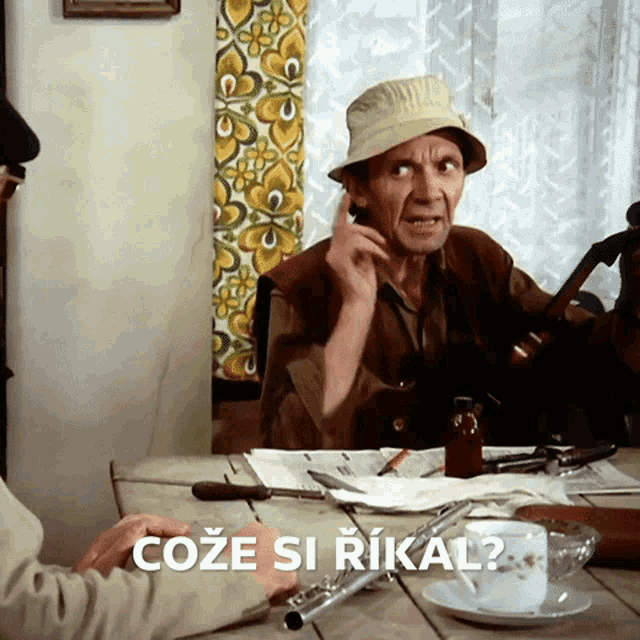 a man in a hat sits at a table with the words coze si rikal written on the table
