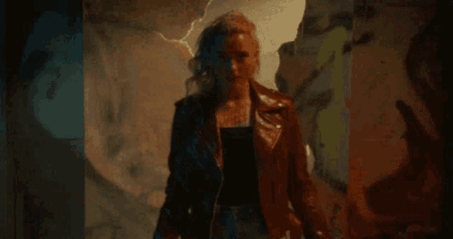 a woman in a leather jacket is standing in front of a wall