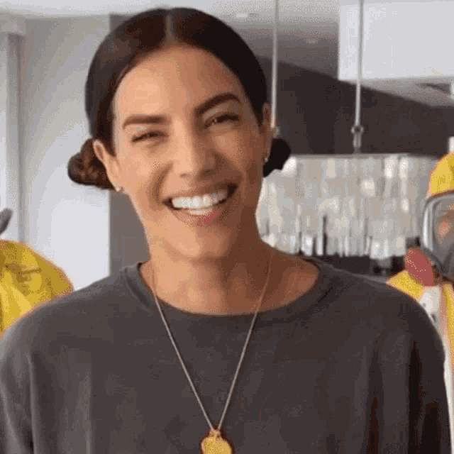 a woman wearing a gray shirt and a gold necklace is smiling for the camera .